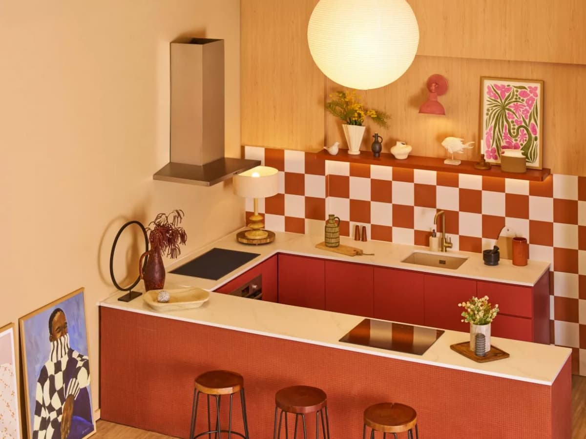 Retro-styled kitchen with terracotta checkerboard tiles, red cabinetry, marble countertop, bar stools, and eclectic artwork — ideal for cooking classes or creative shoot venues