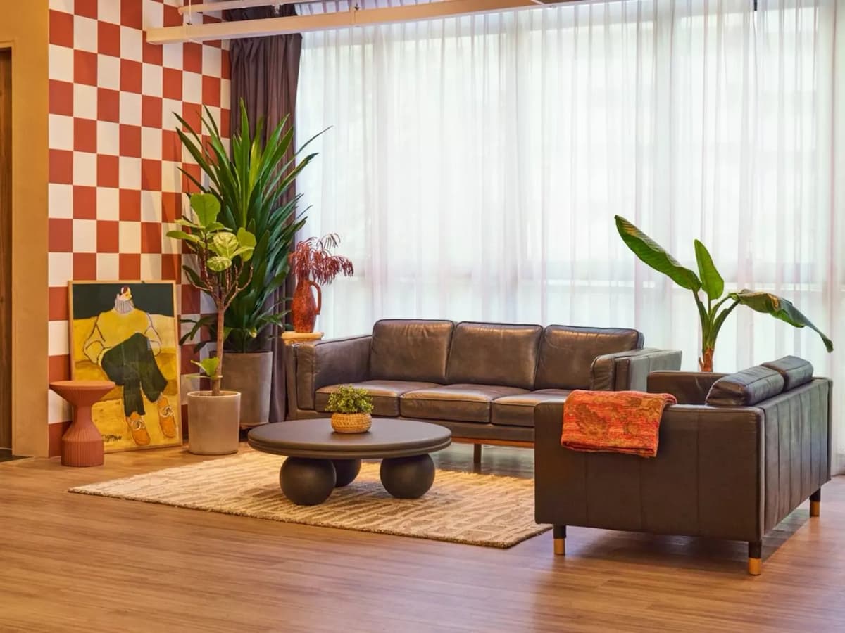 Retro lounge area with brown leather sofas, a round sculptural coffee table, tropical plants, and a terracotta checkerboard feature wall