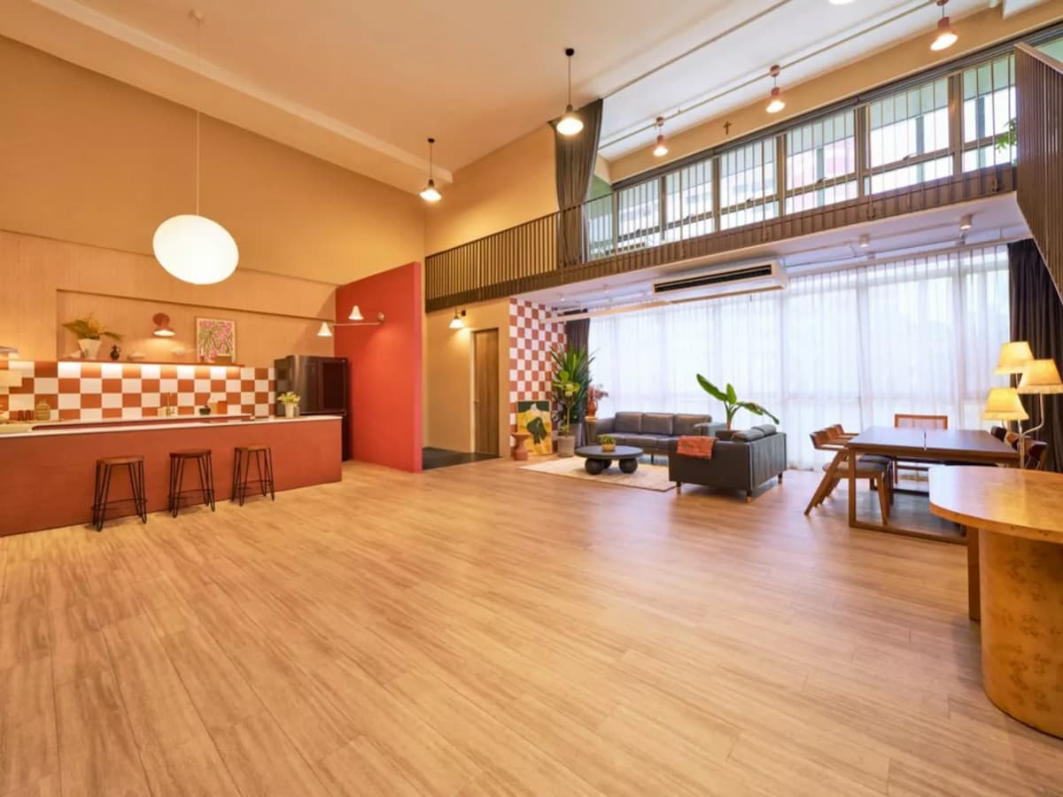 Spacious retro-styled event space with open floor, kitchen bar, lounge seating, mezzanine level, and large windows — suitable for private parties or creative shoots