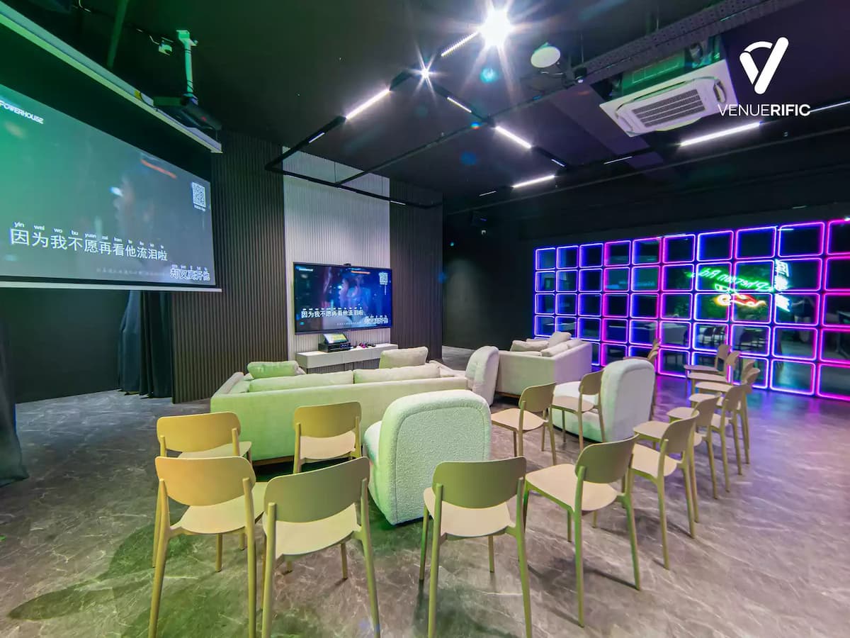 Modern lounge setup with sofas, projector screen, neon-lit wall, and seating for presentations or screenings.