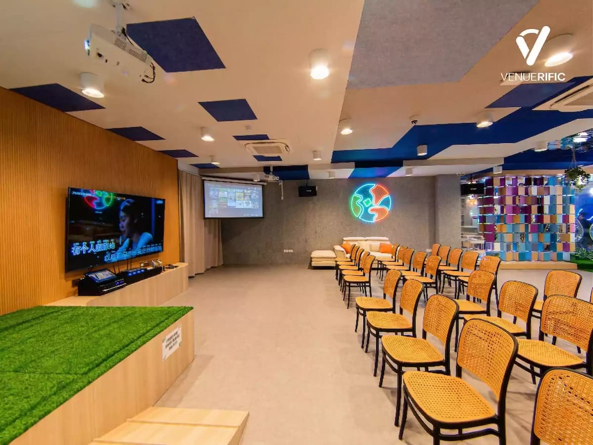 Modern event space with stage, screens, neon wall art, and rows of seating for presentations.