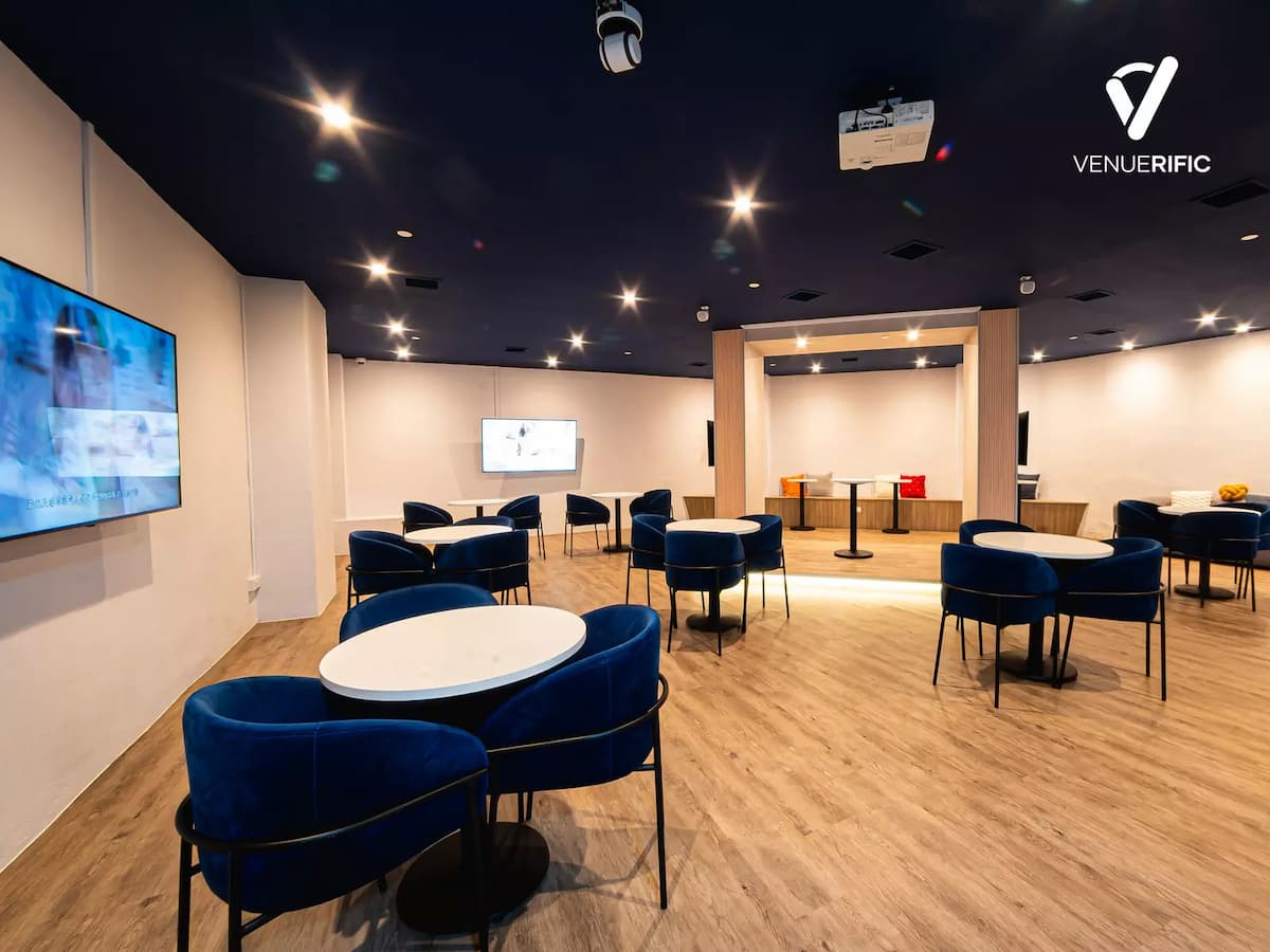 Modern event space with round tables, blue chairs, wall screens, and a central wooden feature area.
