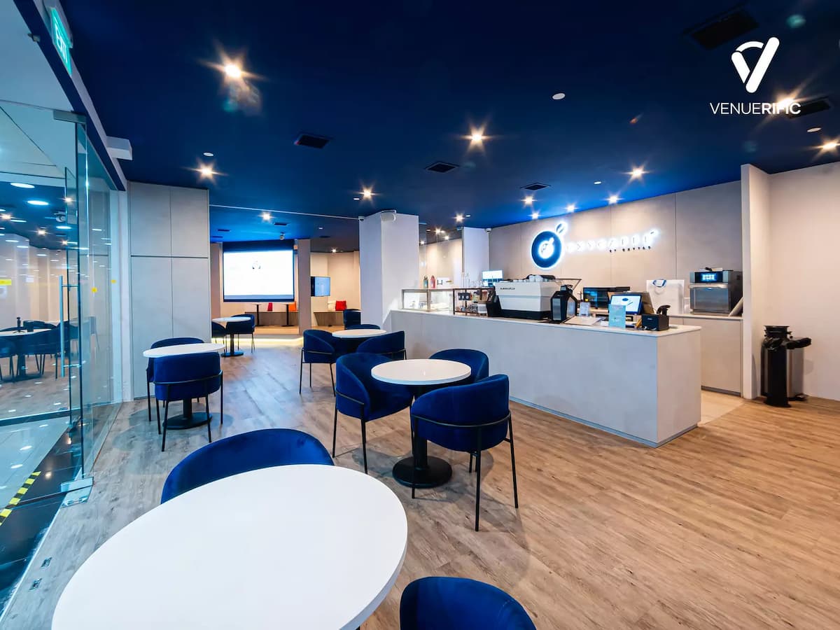 Modern café-style event space with counter bar, blue chairs, round tables, and open seating area.
