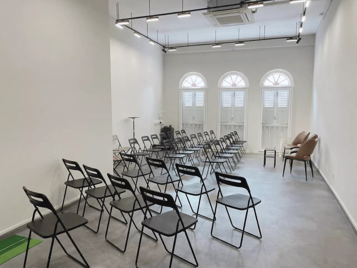 Minimalist event space with rows of chairs, white walls, and natural light from arched windows.