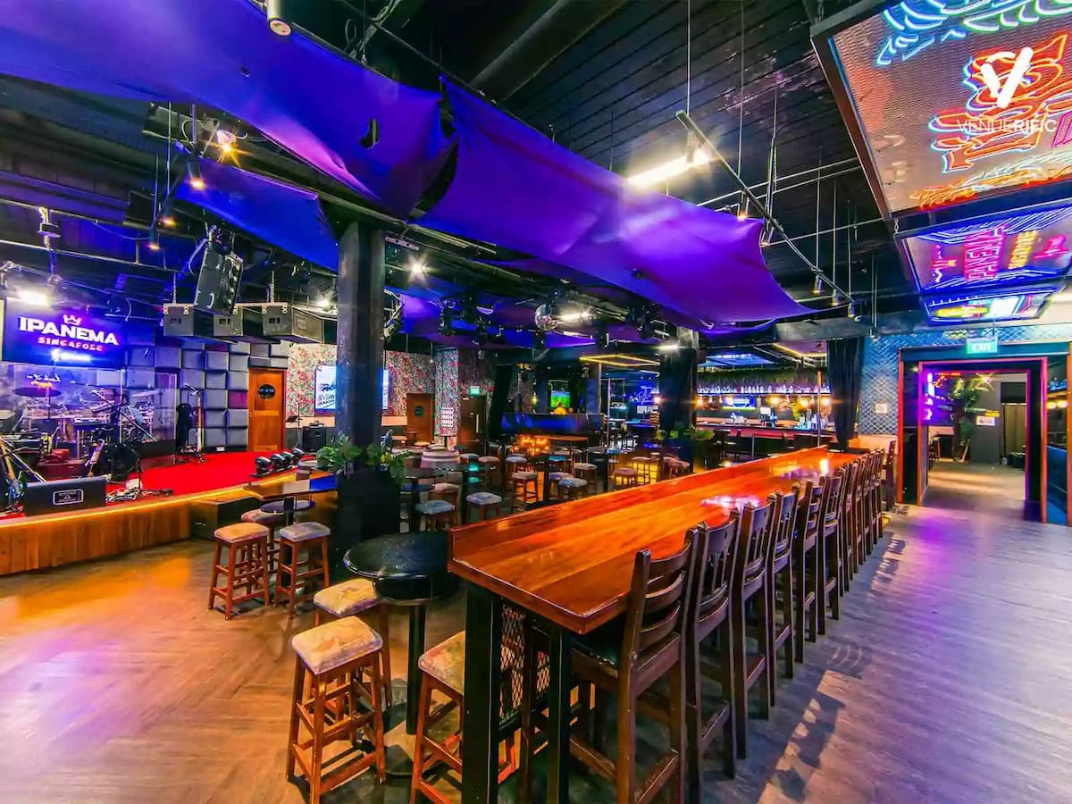 Neon-lit live music venue with long communal seating and stage area.