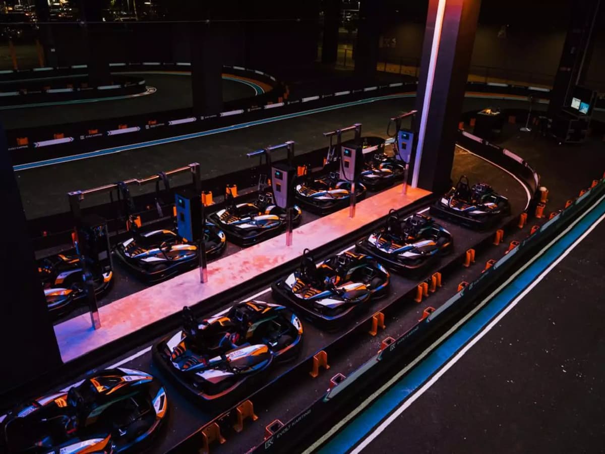 Electric go-karts parked in the charging pit lane beside the indoor racing circuit, ready for upcoming sessions.