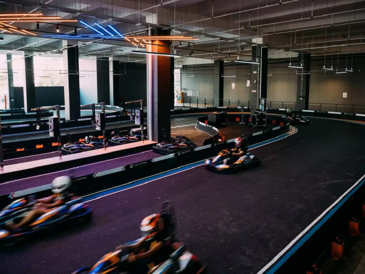 Electric go-karts racing at speed through sweeping corners on a modern indoor karting circuit.