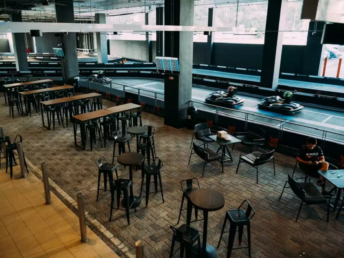 Trackside social dining area with high tables, café seating, and panoramic views of the indoor electric karting circuit.