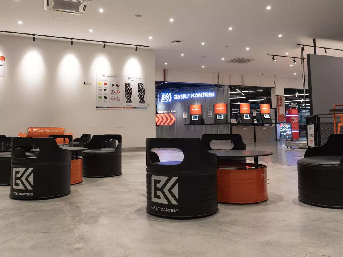 Casual lounge seating area near the self-service registration kiosks and check-in counter at the indoor karting venue.
