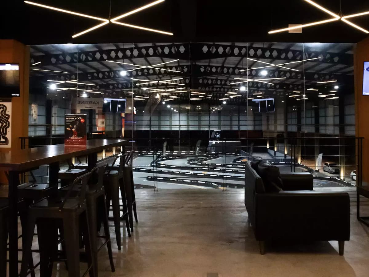 Trackside viewing lounge with bar seating, comfortable sofas, and panoramic views of the indoor karting circuit.