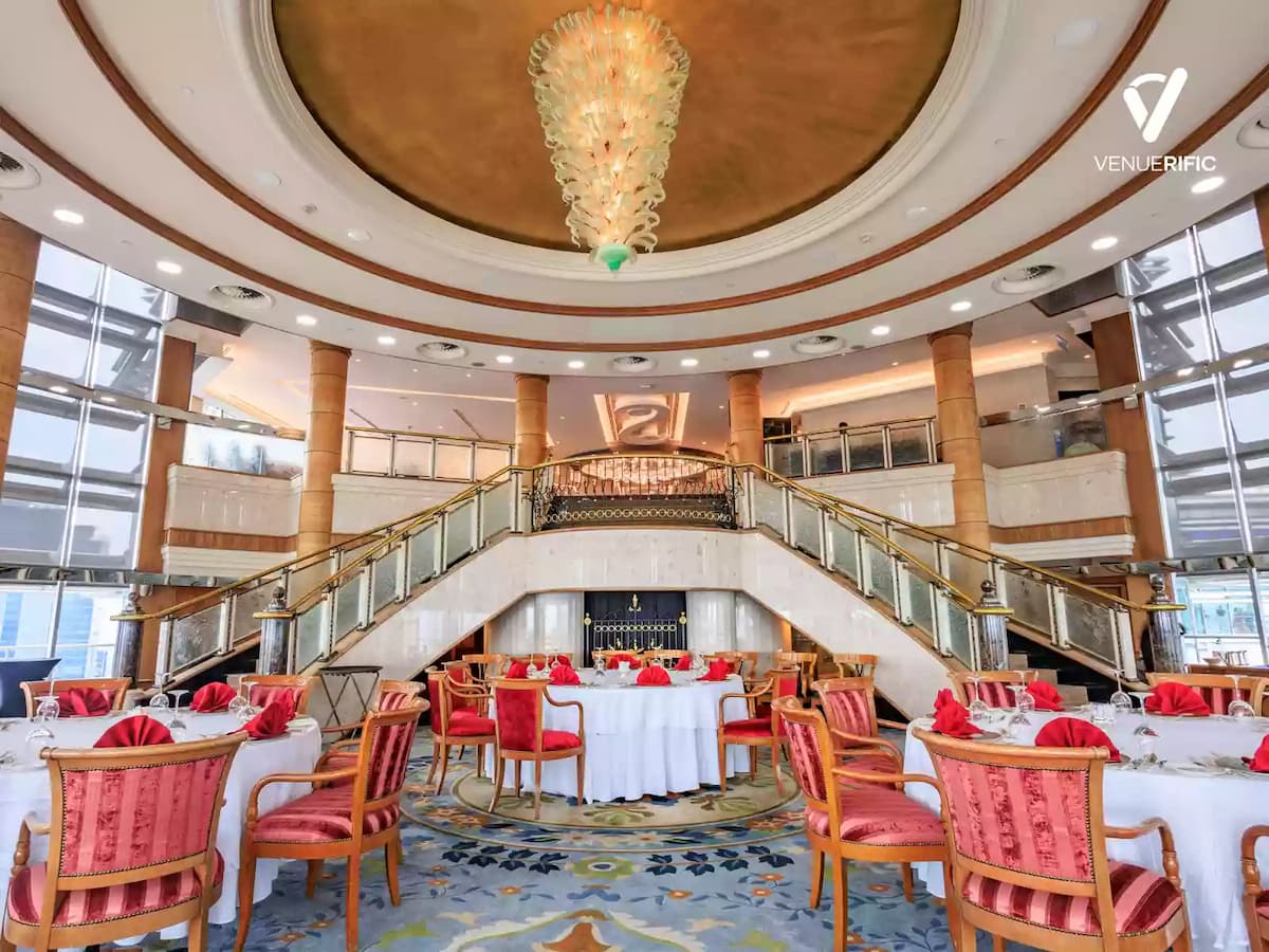 Grand atrium banquet hall with sweeping staircase, round dining tables, and an elegant statement chandelier.