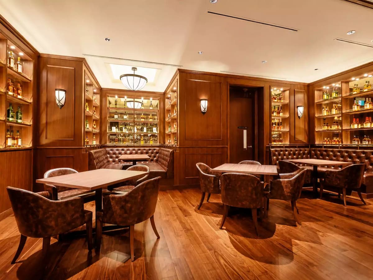 Elegant whisky lounge with leather seating, wood-panelled interiors, and illuminated premium spirits display.