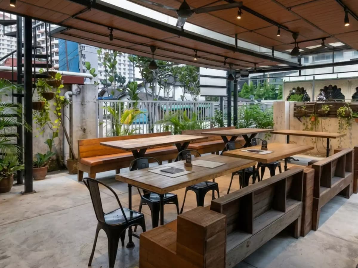 Covered garden terrace with communal wooden tables, bench seating, and lush greenery, ideal for casual dining, team gatherings, and private events.