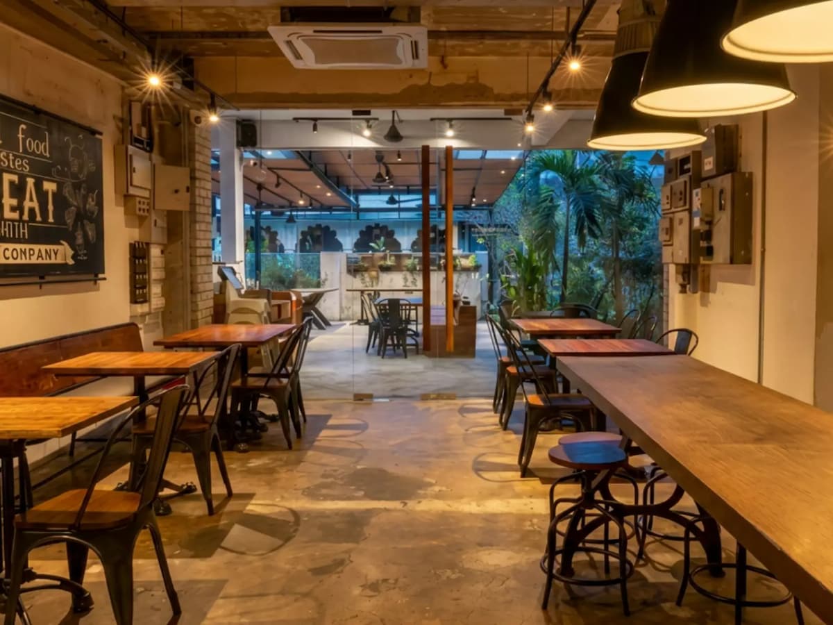 Industrial-style café with communal dining tables, warm lighting, and an open-air terrace, ideal for casual gatherings and private events.