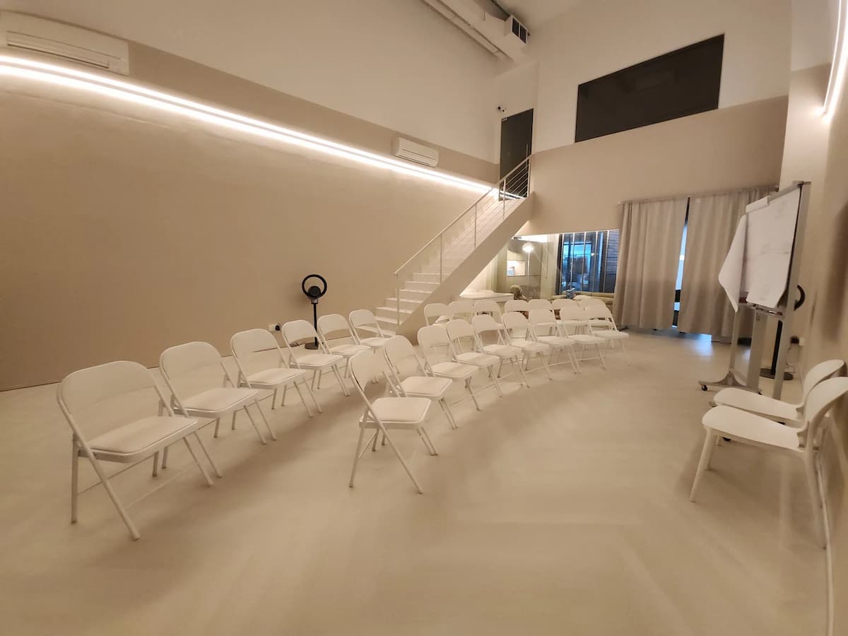 Minimalist event studio arranged in theatre style with white chairs, a presentation area, flip chart, and flexible space for workshops, seminars, and training sessions.