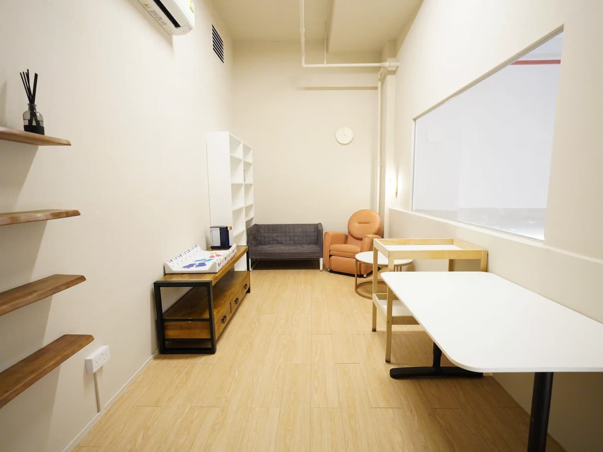 Cozy breakout room with lounge seating, work tables, shelving, and a bright minimalist setting for meetings, collaboration, or event preparation.