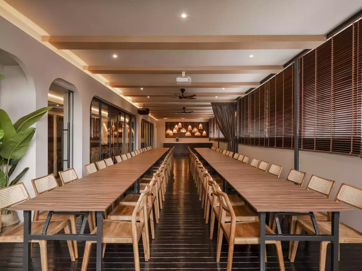 long, wooden table set up in a spacious room with large windows and wooden beams on the ceiling