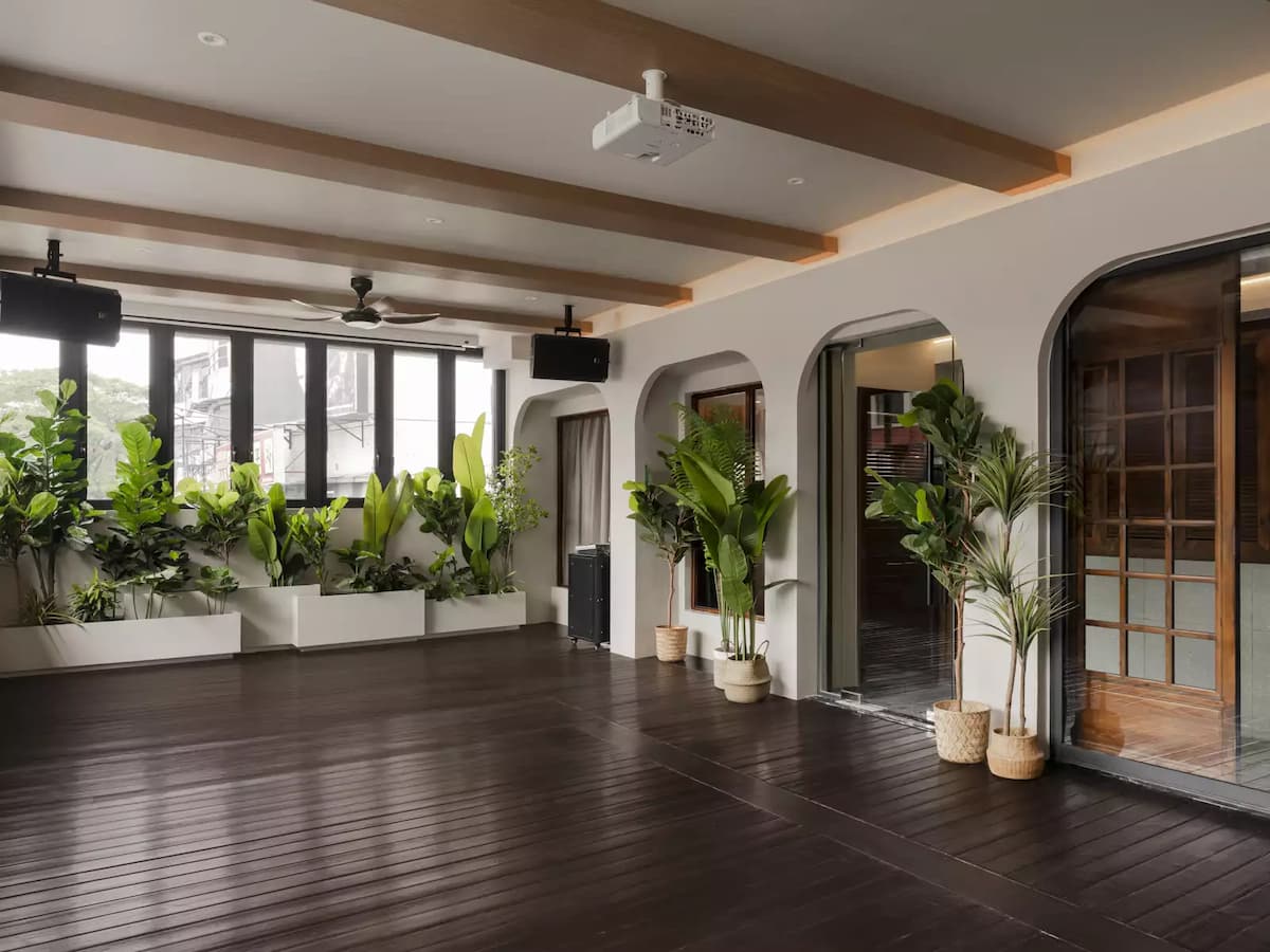 a spacious and modern indoor space with wooden floors, a high ceiling, and large windows overlooking a lush green garden