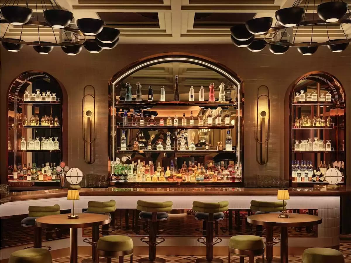 A sophisticated bar with an elegant arched mirror backdrop, warm ambient lighting and plush green seating