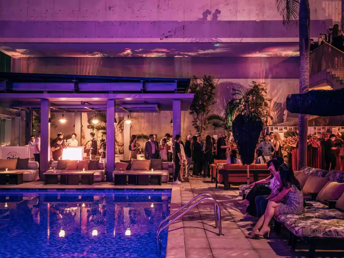 A stylish sky pool party illuminated by vibrant purple and warm ambient lighting, with a fashionable crowd