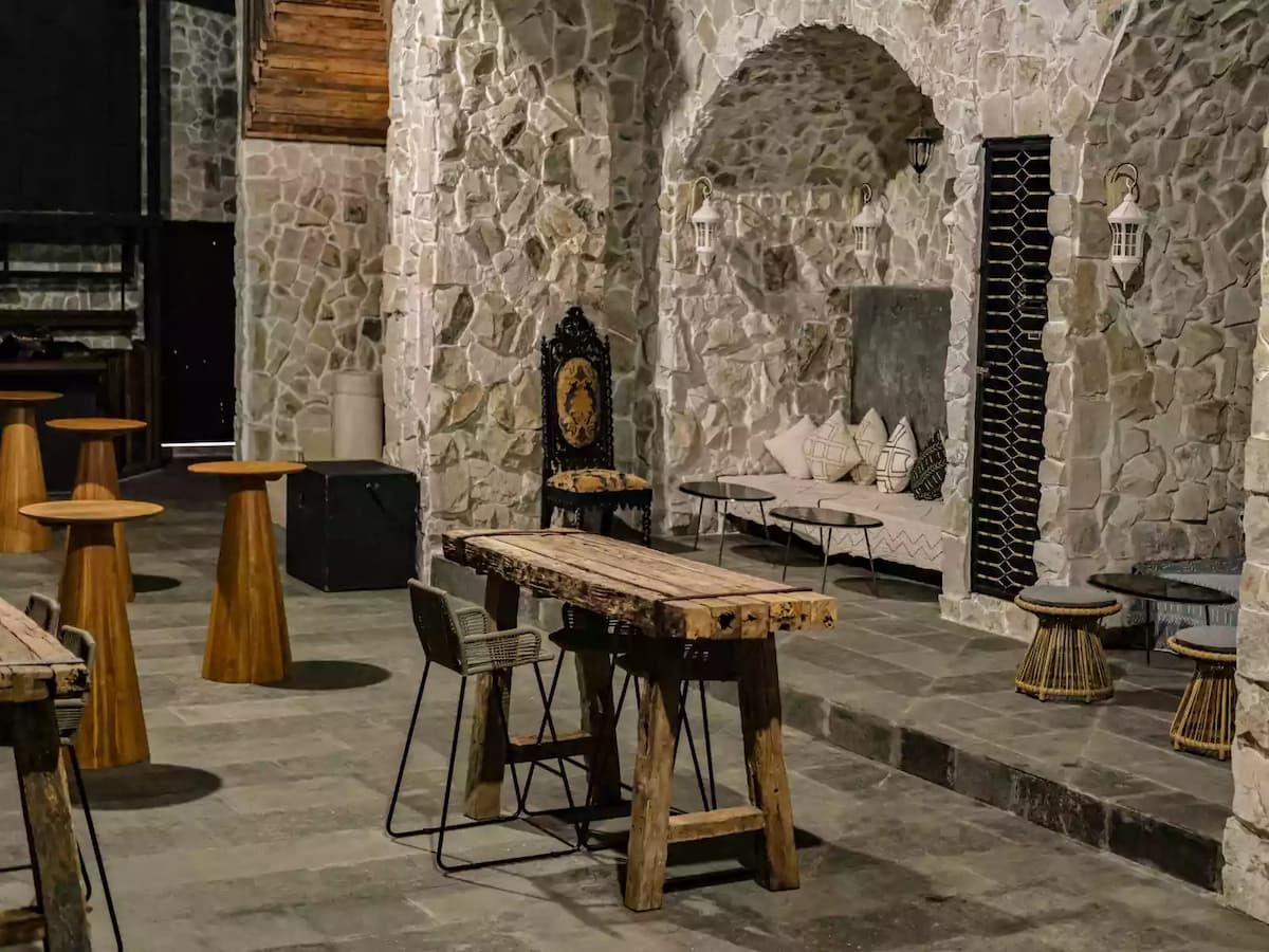 a medieval-inspired lounge with raw stone walls, arched alcoves, and rustic wooden tables