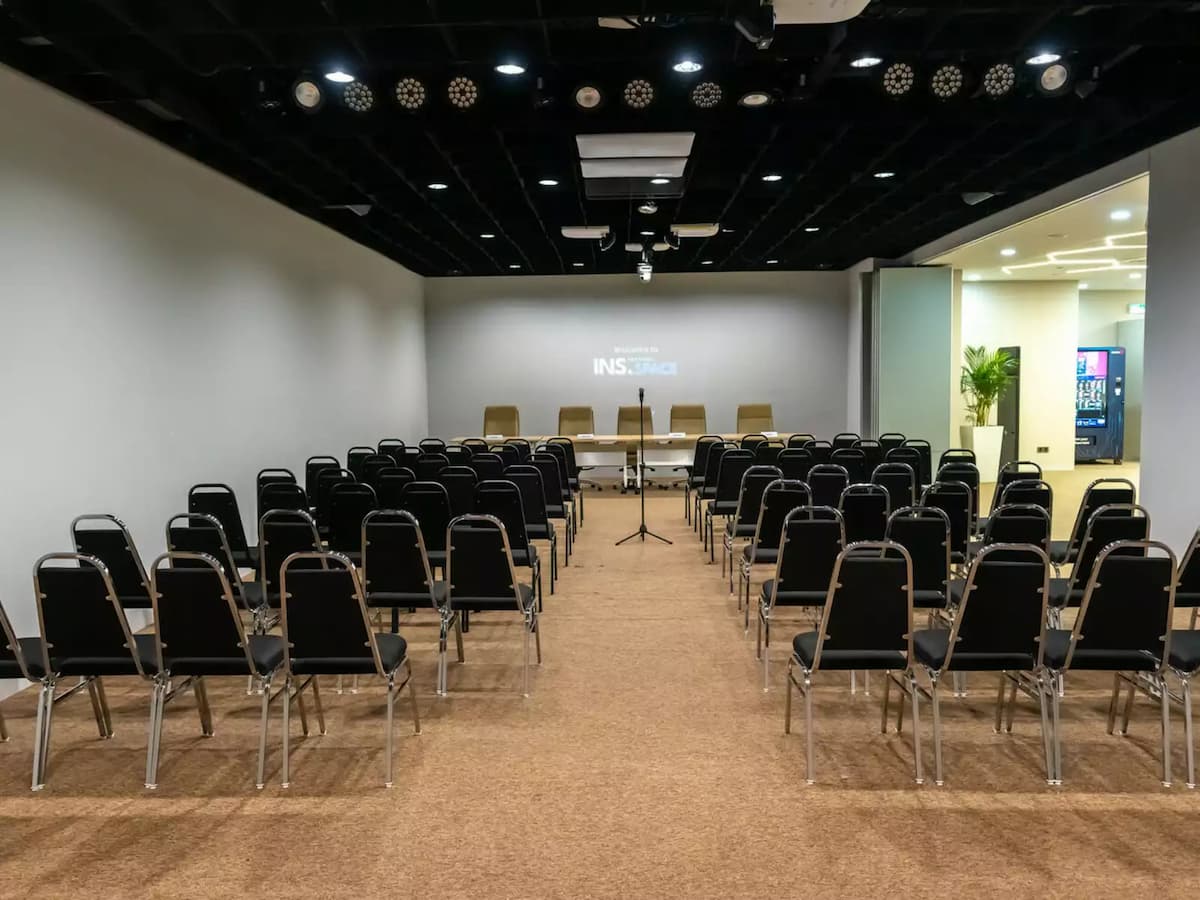 Spacious seminar hall with rows of black chairs facing a stage area, presentation screen, and central podium.