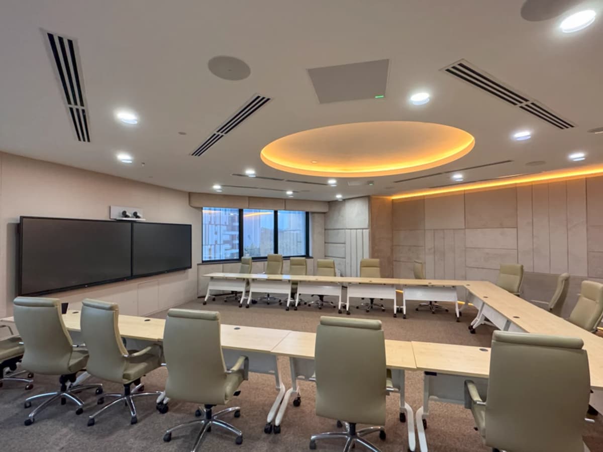 Spacious boardroom with U-shaped conference table, leather chairs, large presentation screens, and warm ceiling lighting.