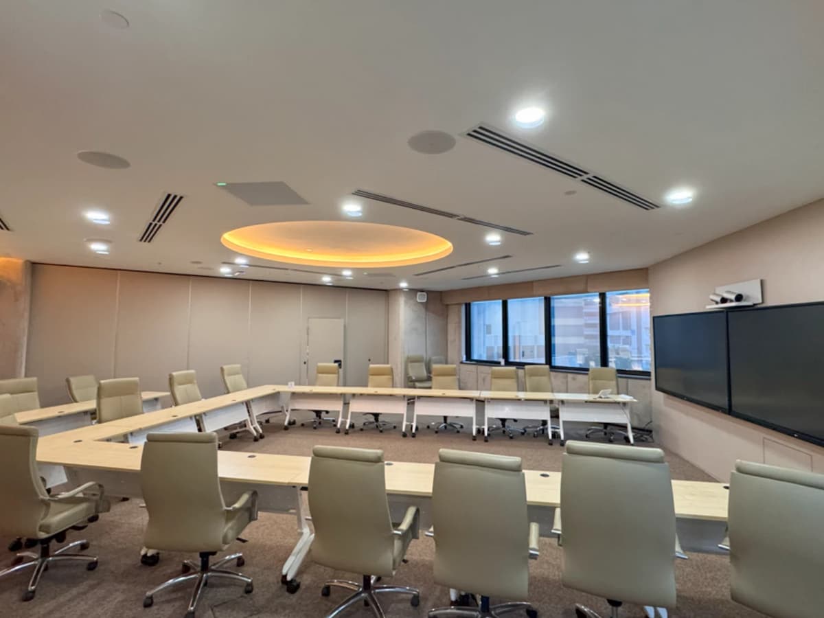 Spacious boardroom with U-shaped conference table, leather chairs, large presentation screens, and warm ceiling lighting.