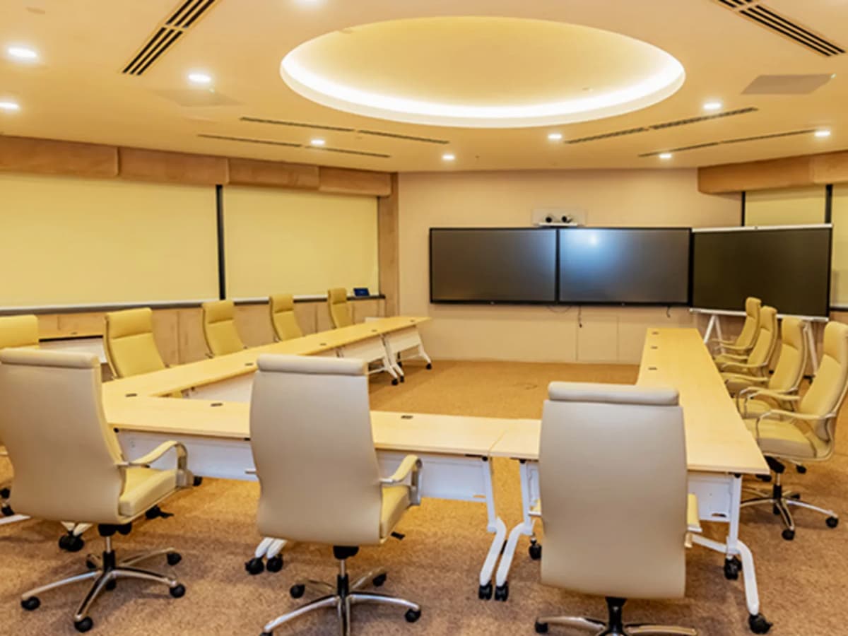 Spacious boardroom with U-shaped conference table, leather chairs, large presentation screens, and warm ceiling lighting.