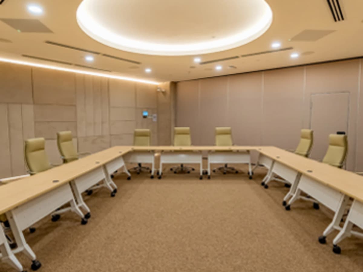 Spacious boardroom with U-shaped conference table, leather chairs, large presentation screens, and warm ceiling lighting.
