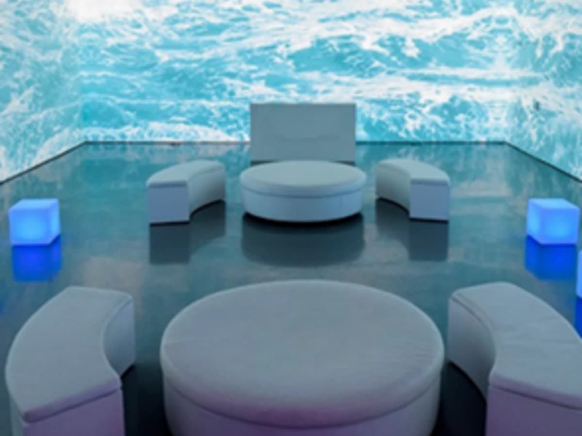 Modern lounge seating with curved white sofas and glowing cube lights set against a digital ocean wave backdrop.