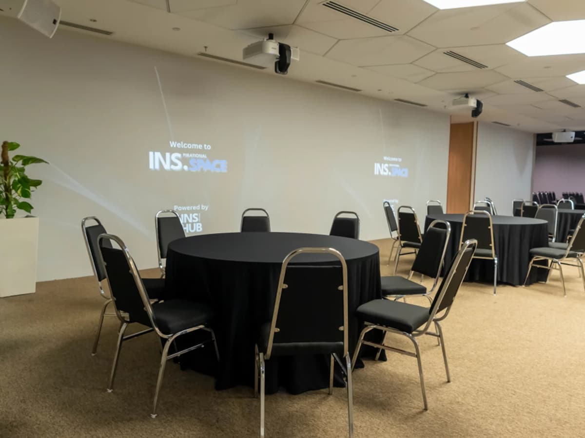 Event hall with round banquet tables, black tablecloths, and projection screens on minimalist walls.