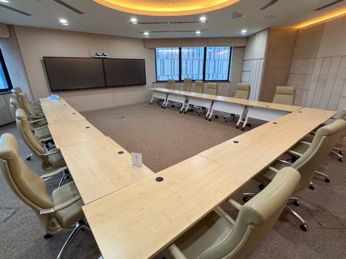 Spacious boardroom with U-shaped conference table, leather chairs, large presentation screens, and warm ceiling lighting.