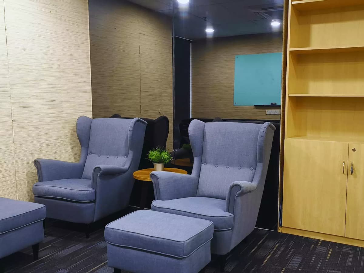 two plush gray armchairs with matching ottomans and a wooden bookshelf against a mirrored wall.