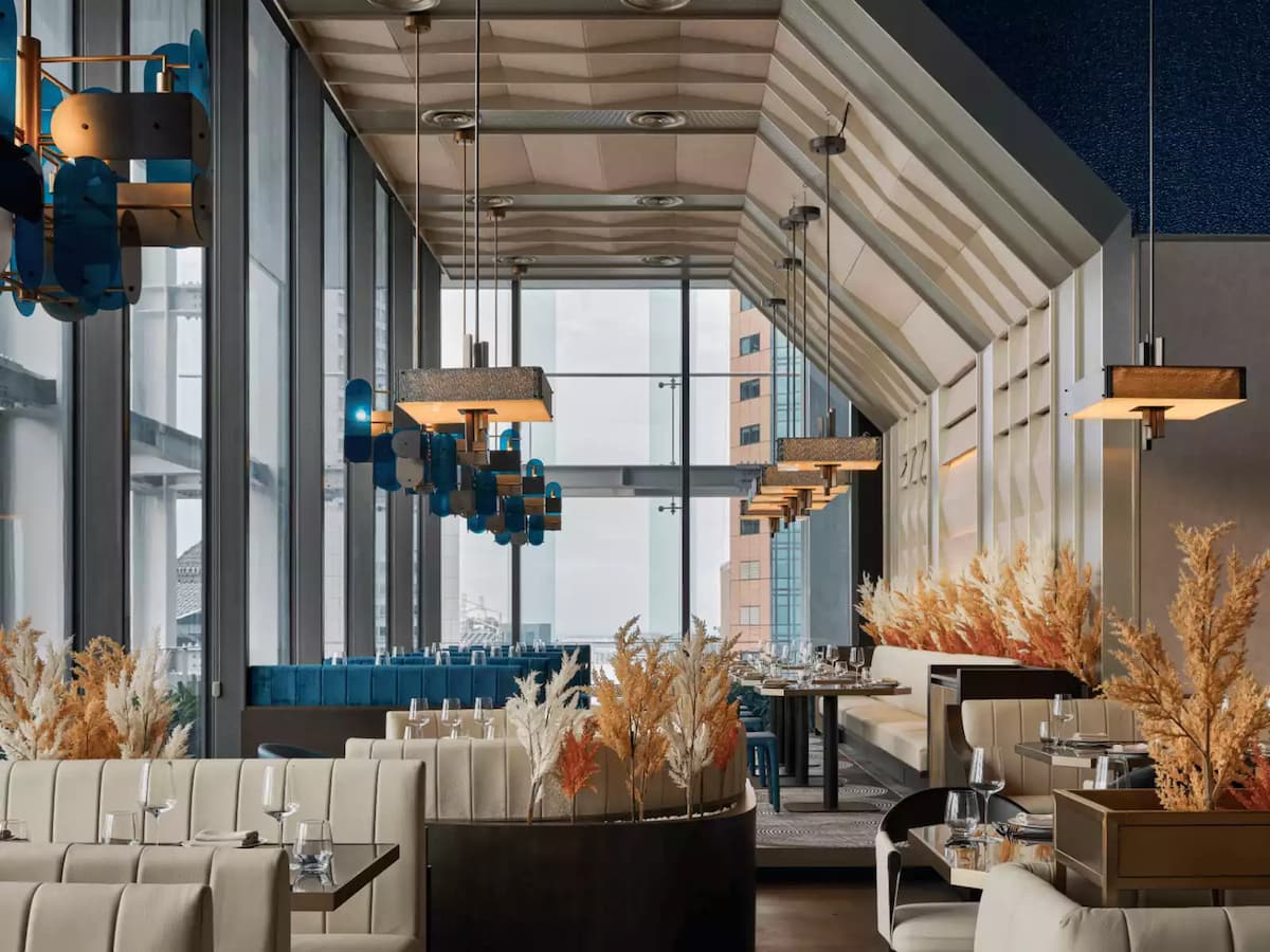 A sophisticated dining area with floor-to-ceiling windows, plush cream seating and warm dried floral accents