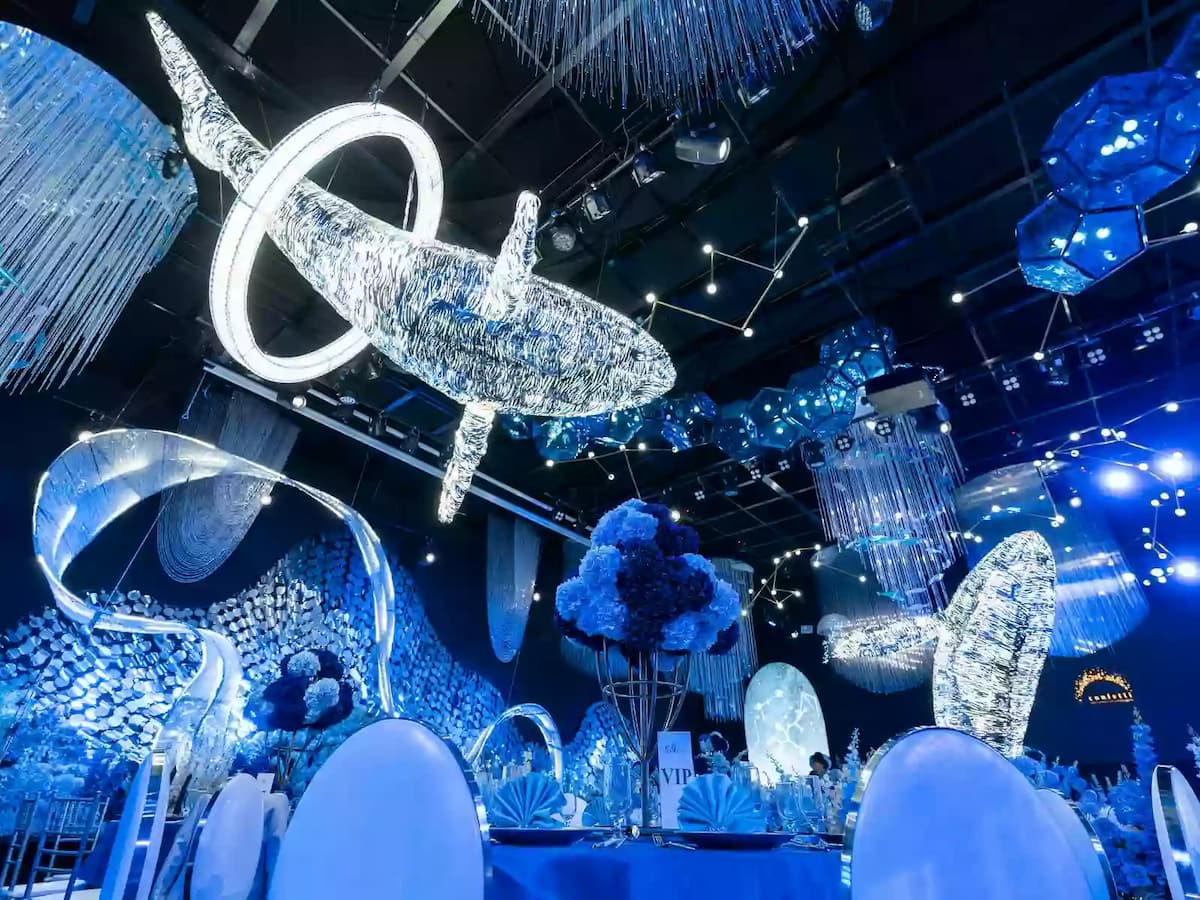 Underwater-themed event hall with illuminated whale sculptures, blue lighting, and elegant banquet tables beneath crystal chandeliers.