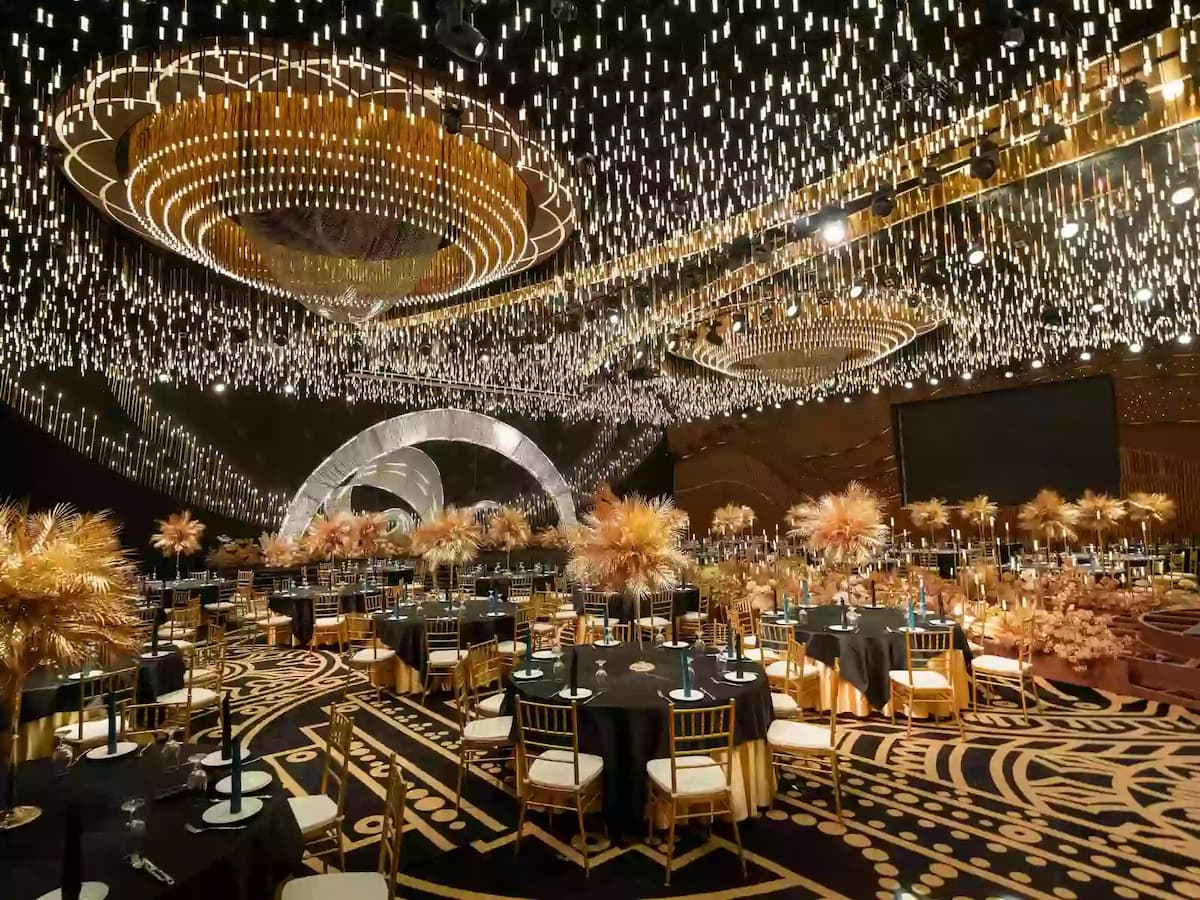 Grand banquet hall with gold chairs, round tables, cascading ceiling lights, and a dramatic stage centerpiece.