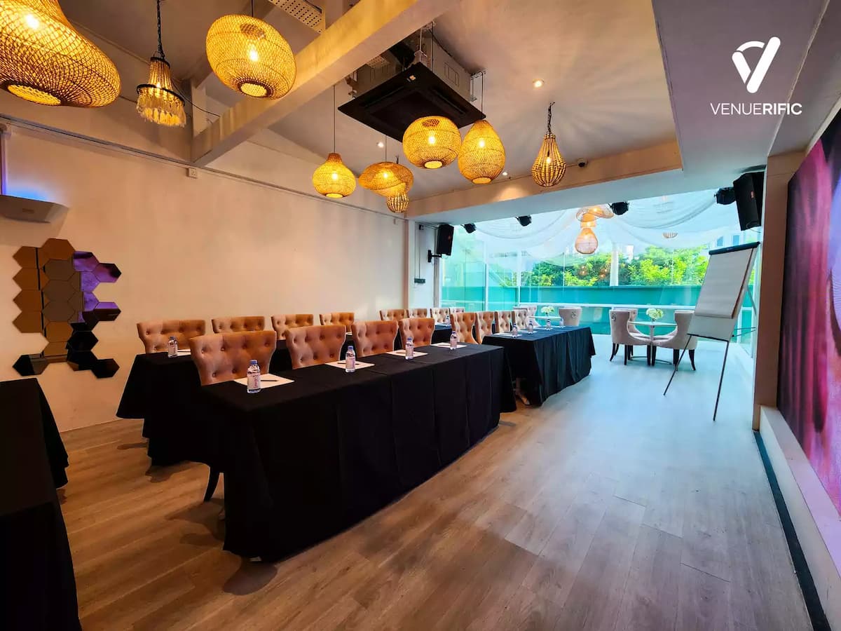 Stylish event venue with tufted seating, black-draped tables for seminar setup, woven pendant lights, and floor-to-ceiling windows overlooking greenery.