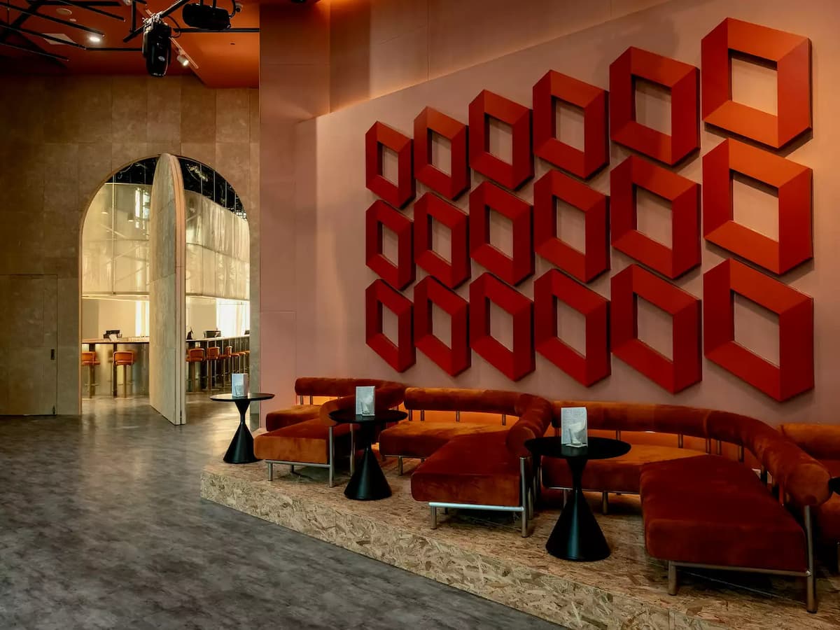 Modern lounge with curved velvet seating, black side tables, and bold red geometric wall art.