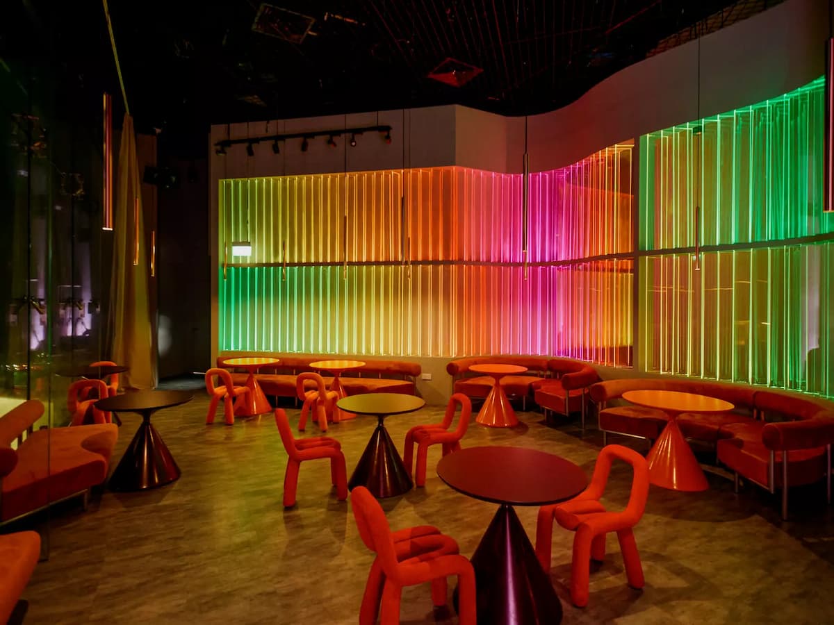 Modern lounge with neon-lit cylindrical feature, red chairs, and city skyline views through glass walls.
