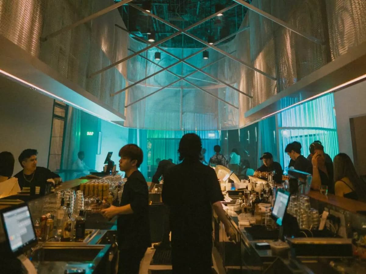Lively bar scene with staff behind the counter, overhead mesh canopy, and teal ambient lighting.