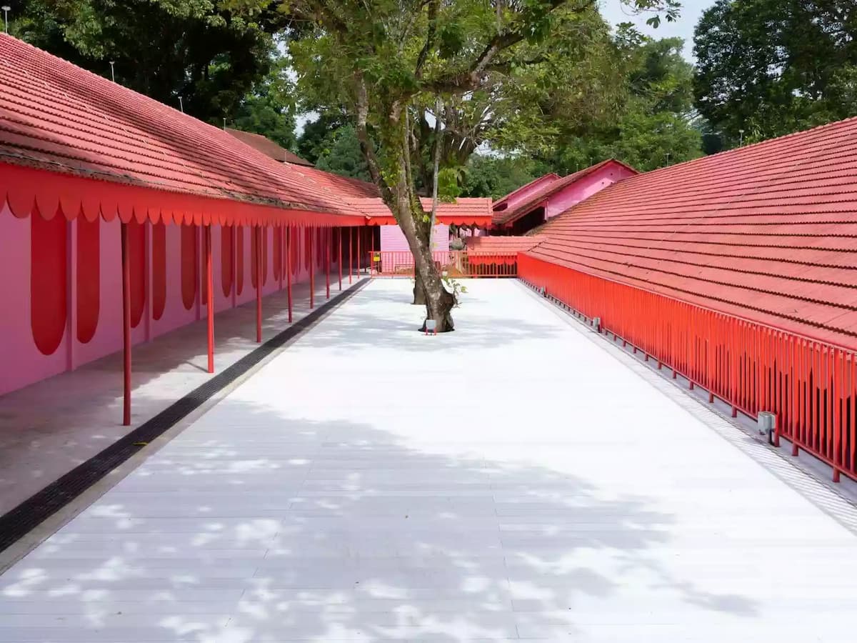 Open courtyard between red-roofed buildings with a central tree and pink architectural details.