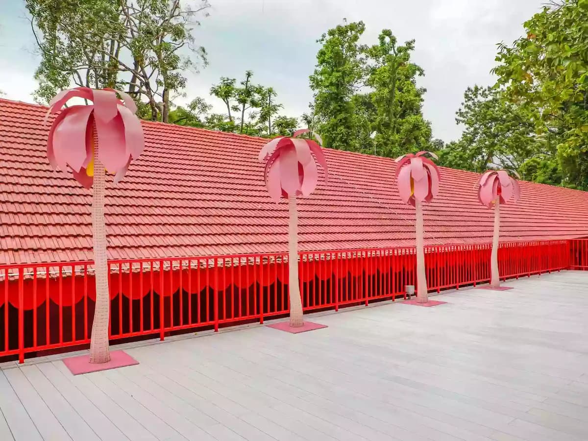 Rooftop terrace with red railings and oversized pink palm tree sculptures against a tiled roof backdrop.