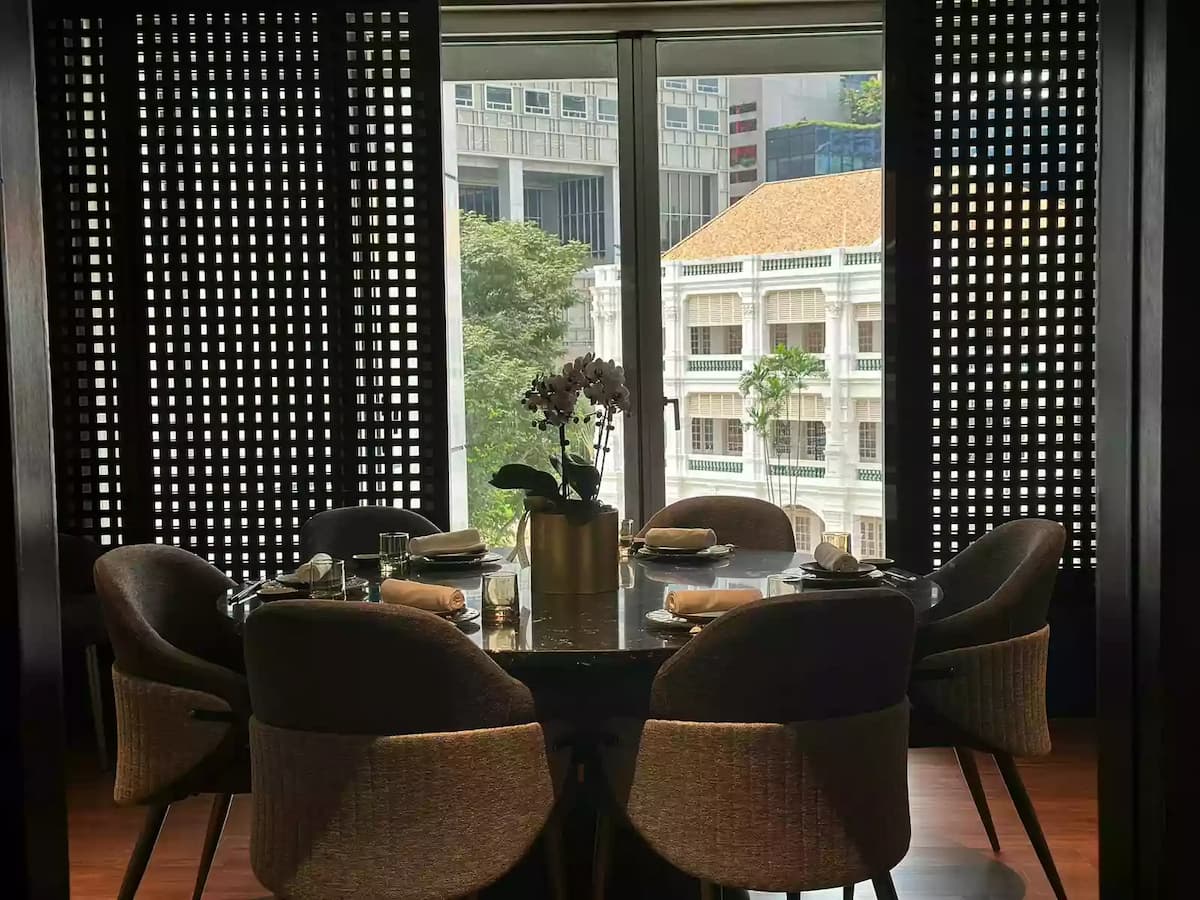 An elegant private dining room featuring a round black marble table set for six, with curved grey upholstered chairs on a warm wood floor