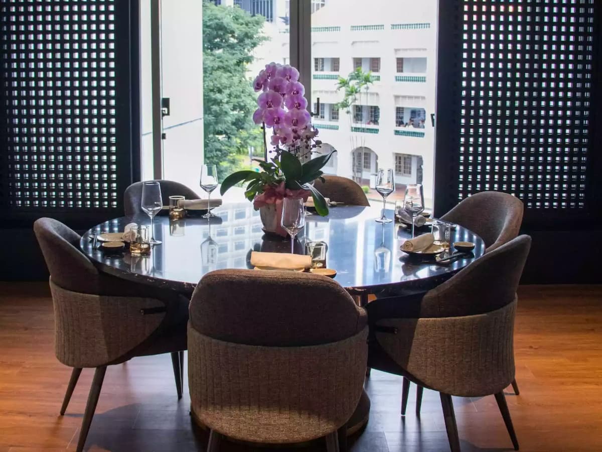 A round, black marble dining table set for six with grey upholstered chairs sits centered in a private room.