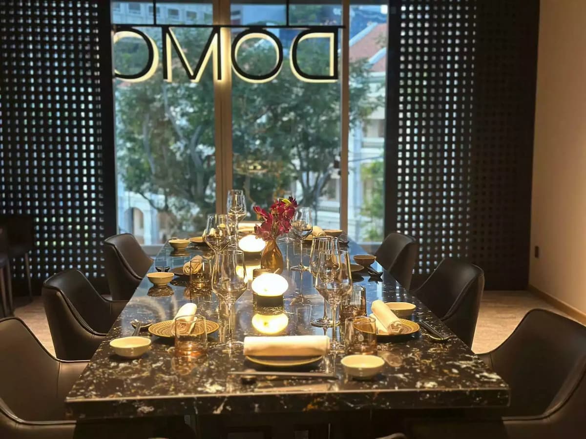 A long, black marble dining table is set for a formal meal with crystal wine glasses, white napkins, and small, glowing table lamps.