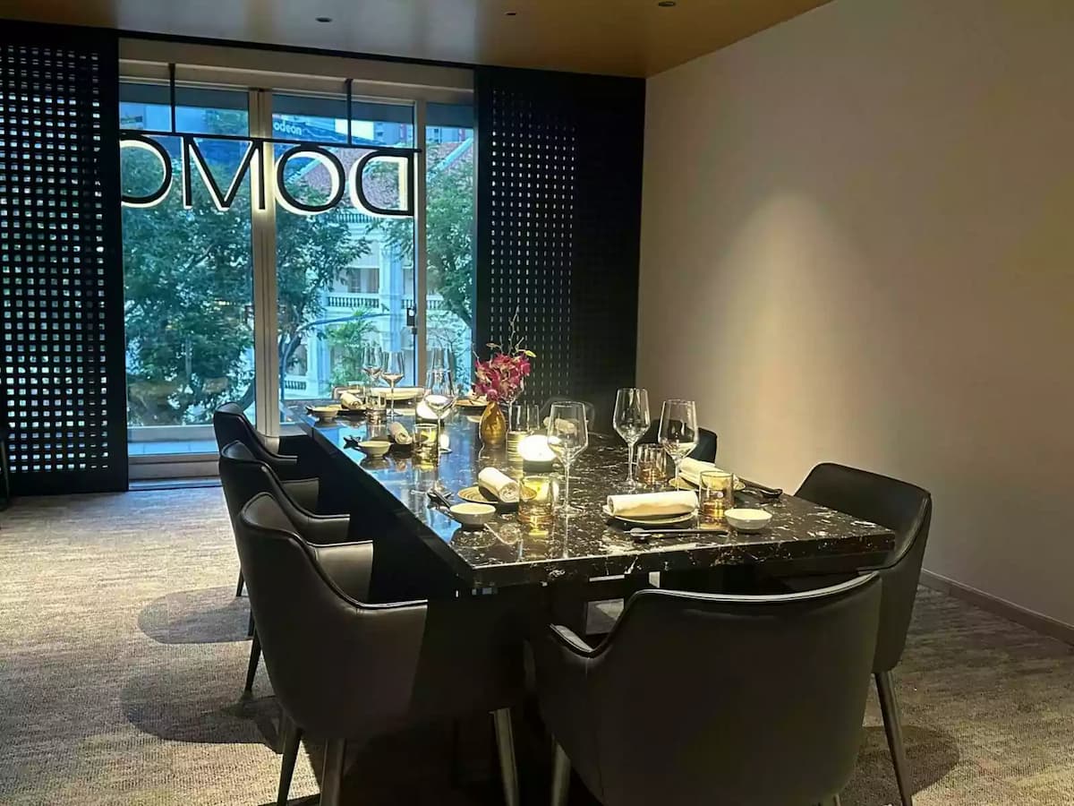 An upscale dining table made of dark, polished marble is set with elegant glassware, white napkins, and small gold lamps.
