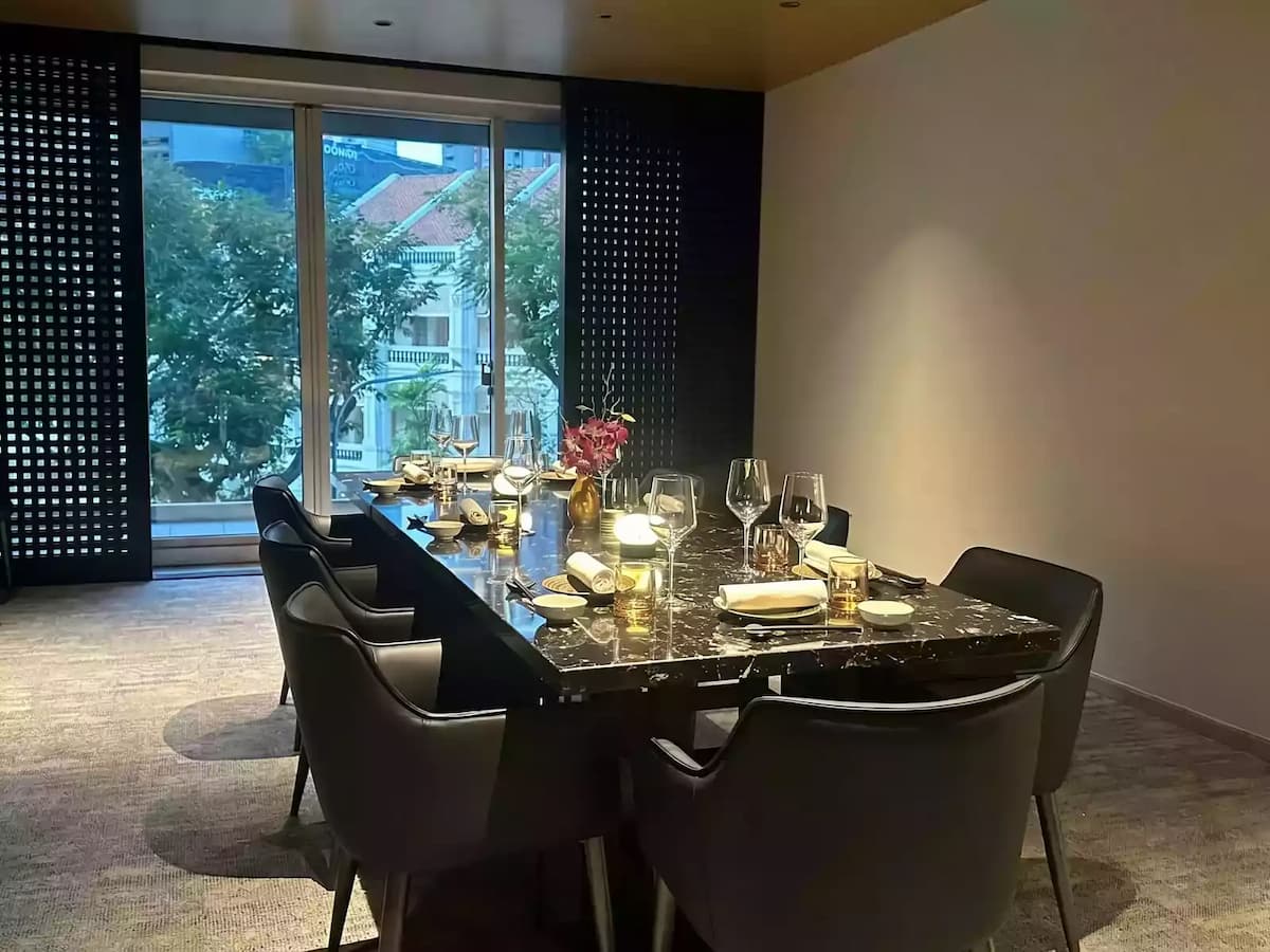 An upscale dining table made of dark, polished marble is set with elegant glassware, white napkins, and small gold lamps.