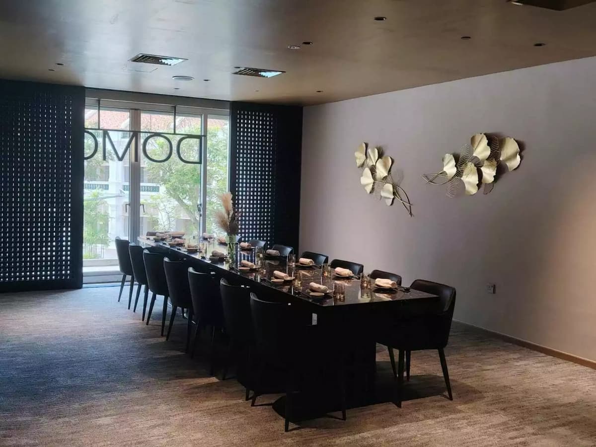 narrow dining room featuring two long, parallel black marble tables set with modern tableware and small, warm lamps.