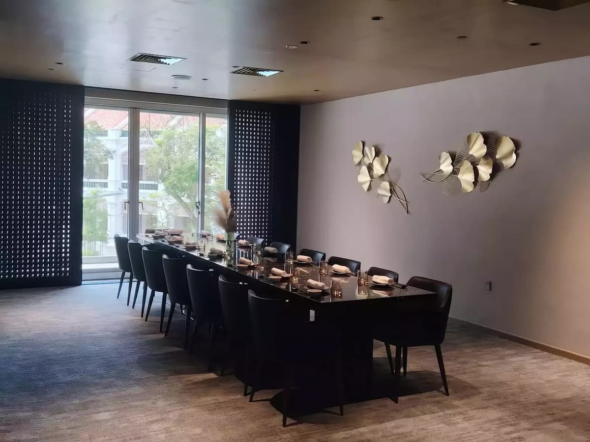 narrow dining room featuring two long, parallel black marble tables set with modern tableware and small, warm lamps.
